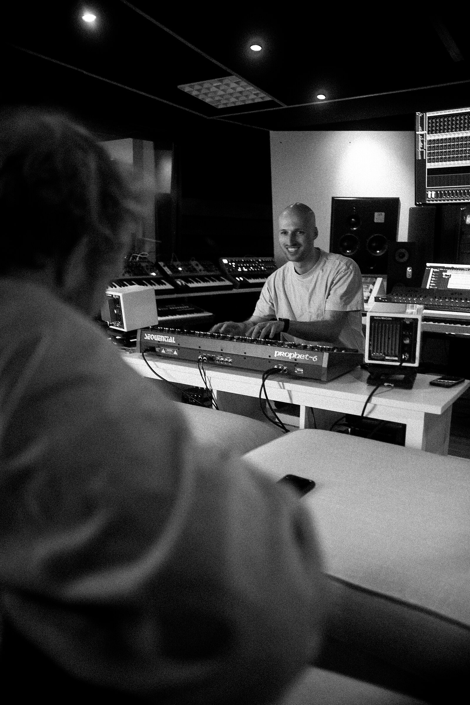 Portraitfoto in schwarz weiß von weißem Mann mitte dreißig mit Glatze, lachend in einem Tonstudio sitzend mit weißem T-shirt.