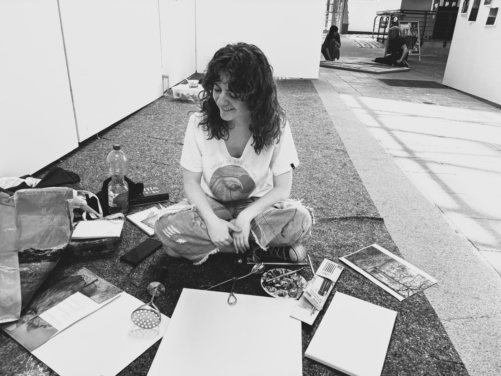 Eine Person mit längeren lockigen HAaren sitzt auf dem Boden, vor ihr liegt Arbeitsmaterial
